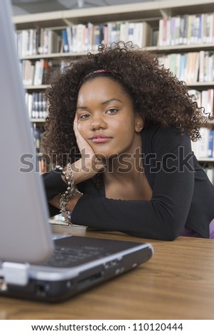 Portrait of a bored African American college student sitting at library desk with laptop