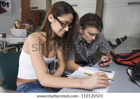 Young female student studying while friend listening to music