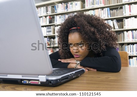 Young African American female student looking laptop screen at library desk