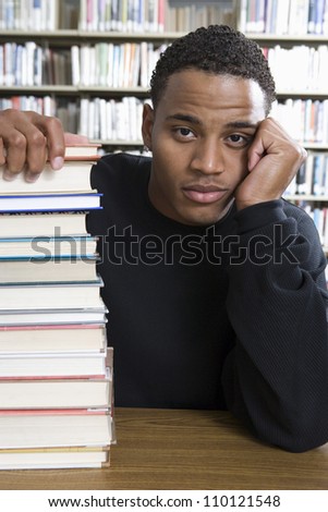 Portrait of a bored African American college student sitting with stack of books in library