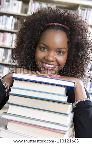 African American female student leaning on stack of books in library