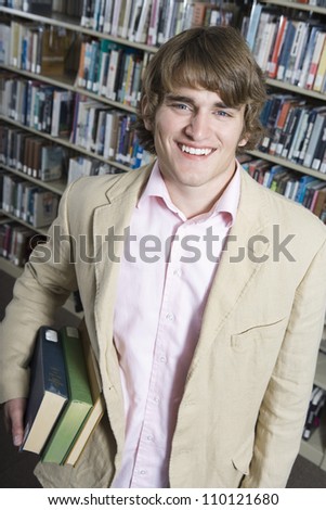 Portrait of a happy male college student holding books in the library