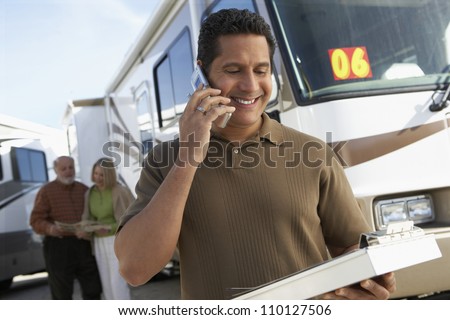Mature tourist guide talking on phone while holding a book with passengers in background