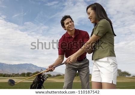 Happy mature man teaching woman to play golf
