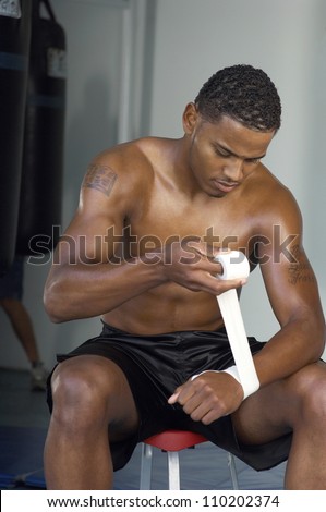 Young boxer wrapping bandage to hand while preparing for a match