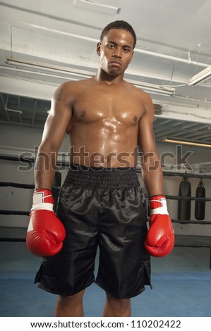 Portrait of a serious male boxer wearing red gloves standing in gym