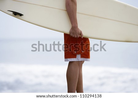 Lower body of young man carrying surfboard on beach