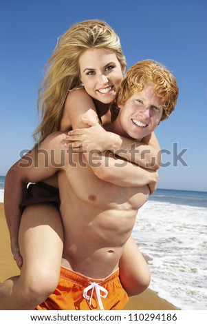 Happy young man carrying woman on beach