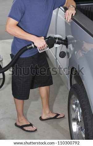 Lower body of a young man refueling his car