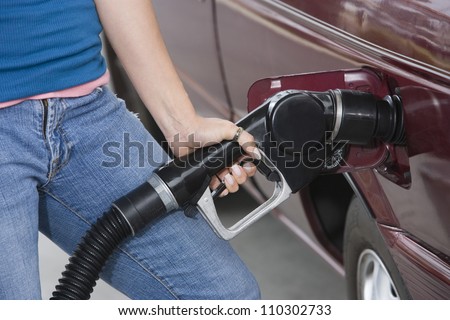 Mid section of a woman refueling her car at a fuel station