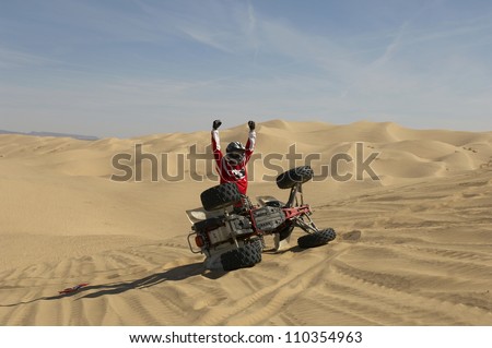 Quad racer cheering tipped-over quad bike in desert