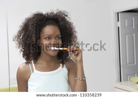 Reflection of African American woman in mirror brushing teeth