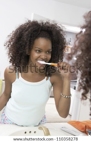 African American woman in mirror brushing teeth