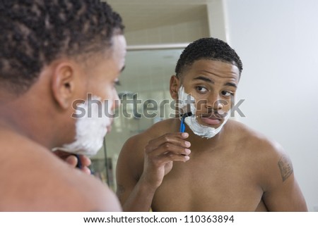 Young man shaving in front of mirror