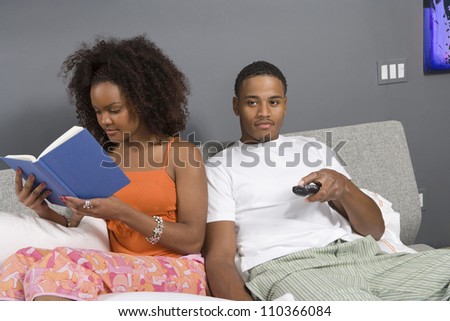 Young man watching TV while woman reading novel in bedroom