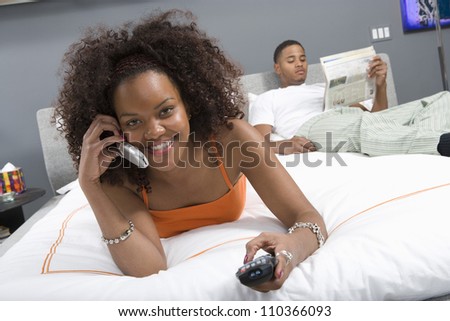 Portrait of young African American woman watching TV with telephone