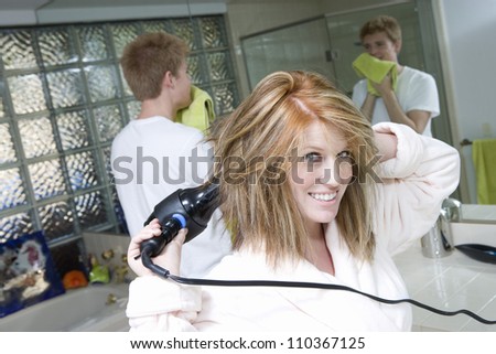 Portrait of woman drying her hair with man in bathroom