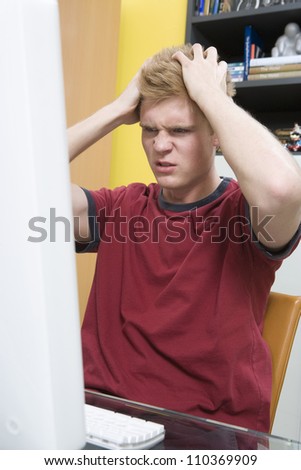 Tensed young man with hands on head looking at computer screen