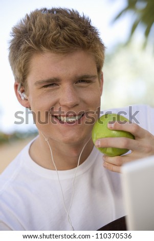 Portrait of happy young man with green apple listening music