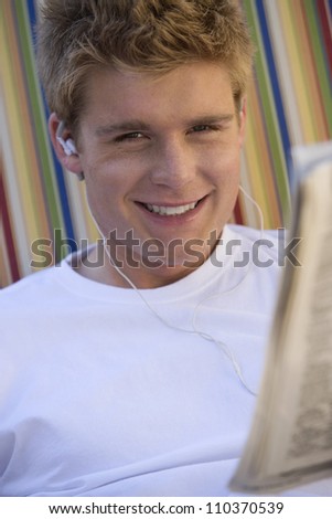 Portrait of a happy young man reading newspaper while listening music