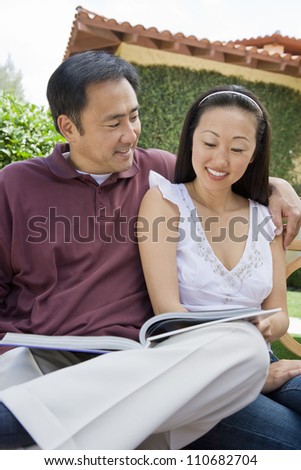 Happy middle aged couple reading novel outdoors