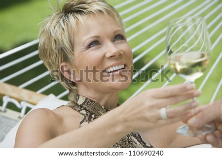 Happy middle age woman holding wine glass on hammock
