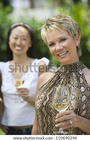 Happy middle aged woman holding wine glass with female friend
