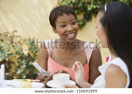 Happy African American woman holding cell phone while chatting with female friend