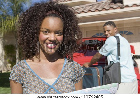 Portrait of happy African American woman with man keeping luggage in car