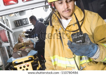 Fire worker holding walkie-talkie with patient and EMT doctor in the background