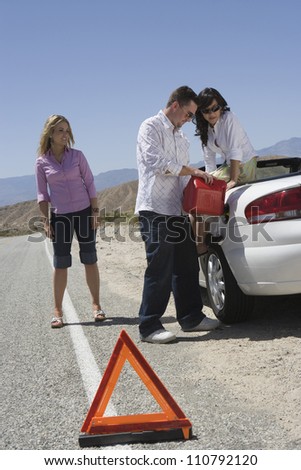 Full length of friends refueling car with warning triangle in the foreground
