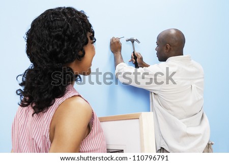 African American couple hammering nail into wall to hang picture frame