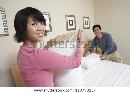 Portrait of happy woman with man arranging bed sheet