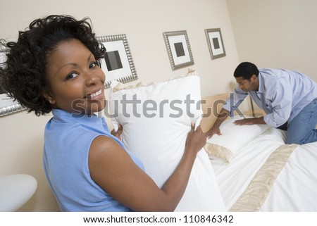 Portrait of an African American woman holding pillow with man arranging bed at home