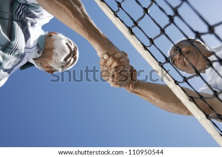 Low angle view of senior tennis players shaking hands against clear sky
