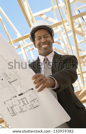 Portrait of a happy engineer holding blueprint at construction site