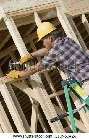Man using a hammer to nail a wood at construction site