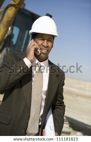 African American architect wearing hard hat as he\'s on call at construction site