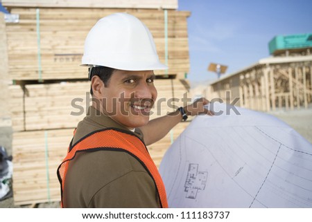 Smiling architect with blueprint at construction site