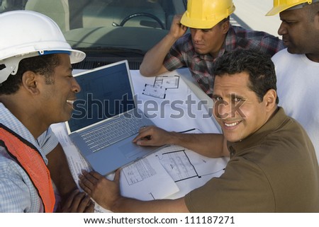 Happy architect and builders discussing with laptop at construction site