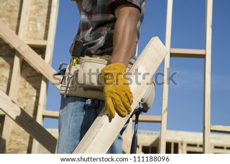 Mid section of a worker carrying materials at a construction site