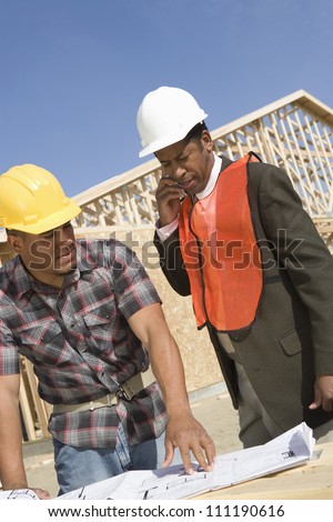 Architect phoning with co-worker standing by at construction site
