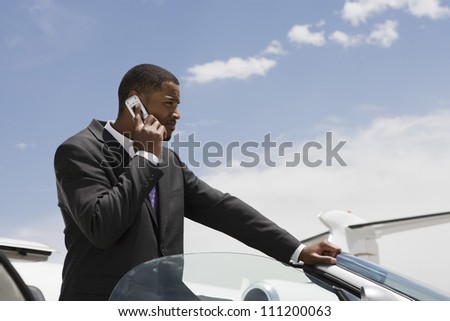Young African American businessman on a call by car at airfield