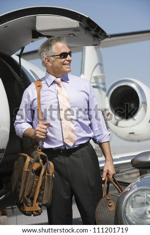Senior happy businessman standing by airplane with luggage at airfield