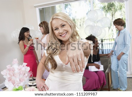 Portrait of a beautiful young bride showing her engagement ring with friends in the background