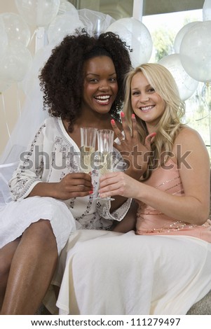 Portrait of happy female friends holding champagne flute and showing nail polish