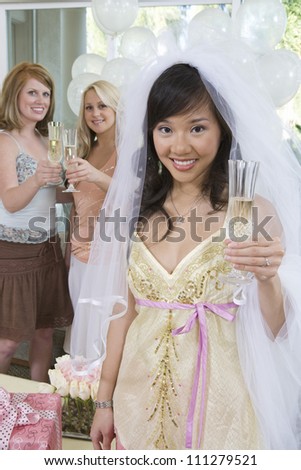 Portrait of young happy bride holding champagne flute with friends in the background