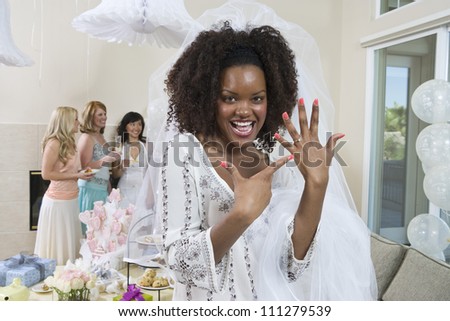Portrait of an excited bride showing her engagement ring with friends celebrating  party in the background