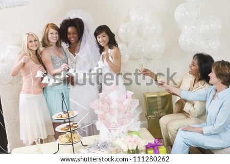 Portrait of bride and her friends holding wedding bells with women toasting champagne at party