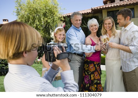 Teenage boy recording happy moments of family celebrating together at garden